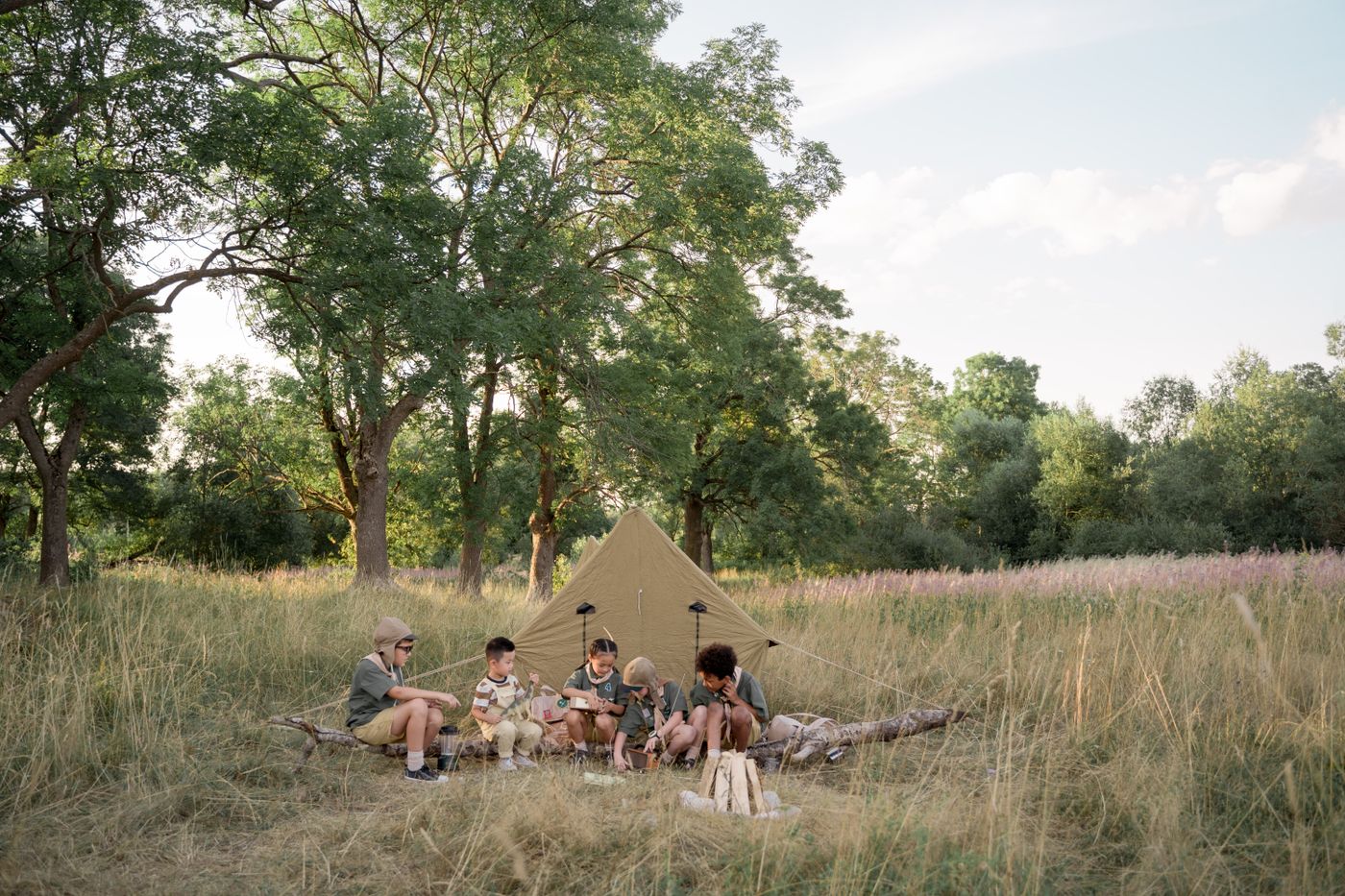 Children sitting by a tent at an outdoor camp.